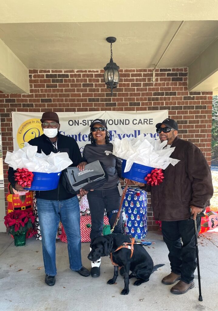 Left to right, Dr. Jay McLeod, Yoneka Trent with guide dog Tavi, and Ronnie Moore holding gift baskets of necesseties.