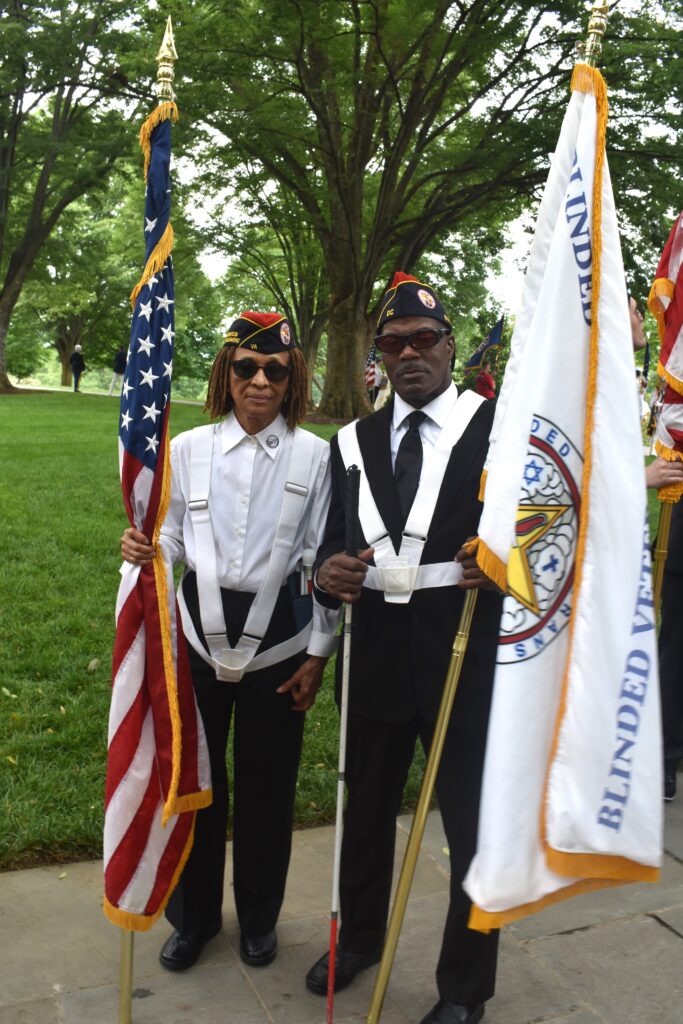 Carol standing with the US flag and Lawrence standing with the BVA flag.