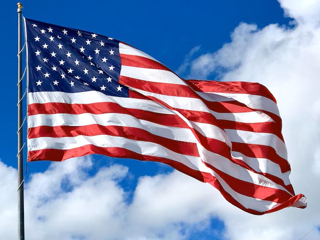 A US flag waving in the wind against a blue sky with white fluffy clouds