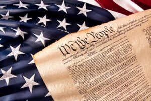 An American Flag as the background with a print of the Constitution with "We the people" visible