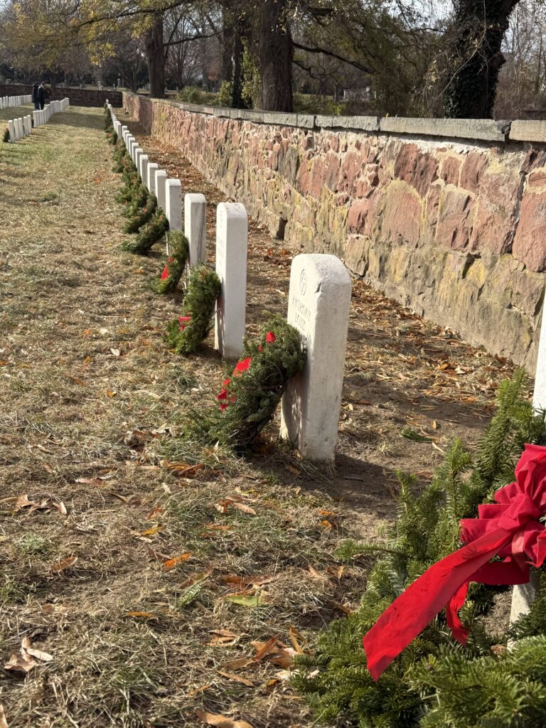 Photograph of a military cemetery row featuring white headstones adorned with green wreaths decorated with red bows.